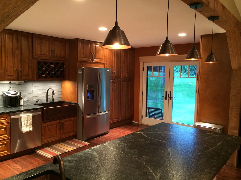 Eat-in kitchen - large rustic l-shaped medium tone wood floor eat-in kitchen idea in St Louis with a farmhouse sink, raised-panel cabinets, granite countertops, gray backsplash, glass tile backsplash, stainless steel appliances and a peninsula