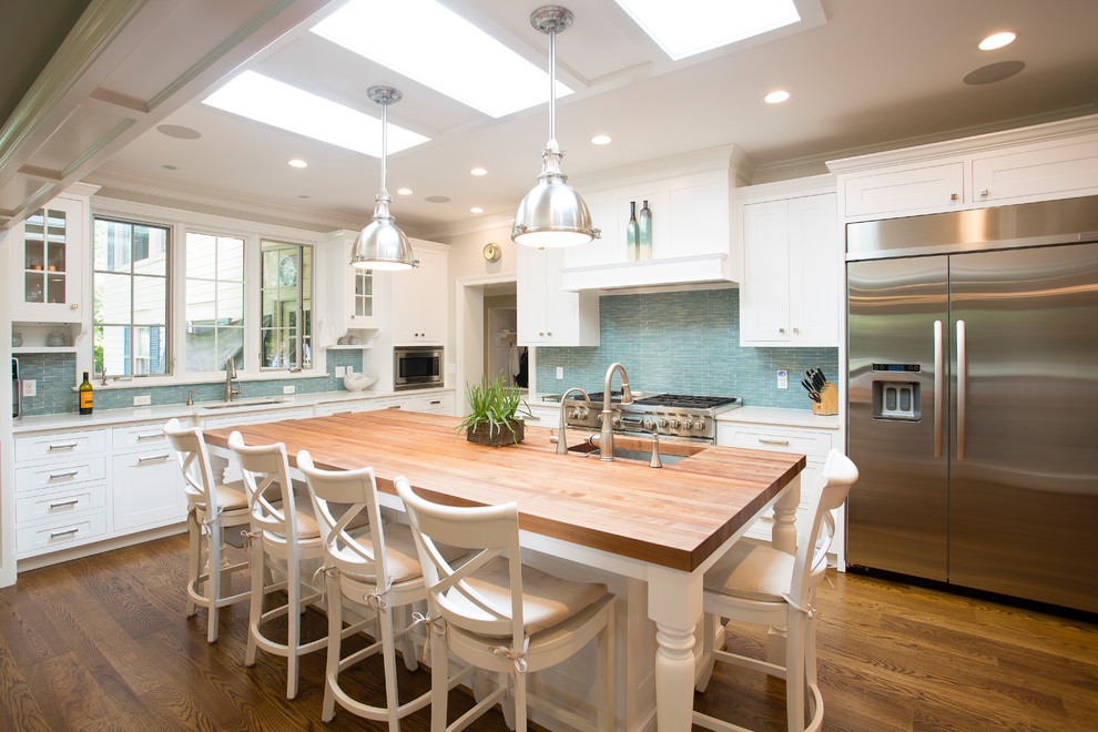 Photo of a large beach style l-shaped separate kitchen in DC Metro with an undermount sink, shaker cabinets, white cabinets, wood benchtops, blue splashback, glass tile splashback, stainless steel appliances, dark hardwood floors, with island and brown floor.