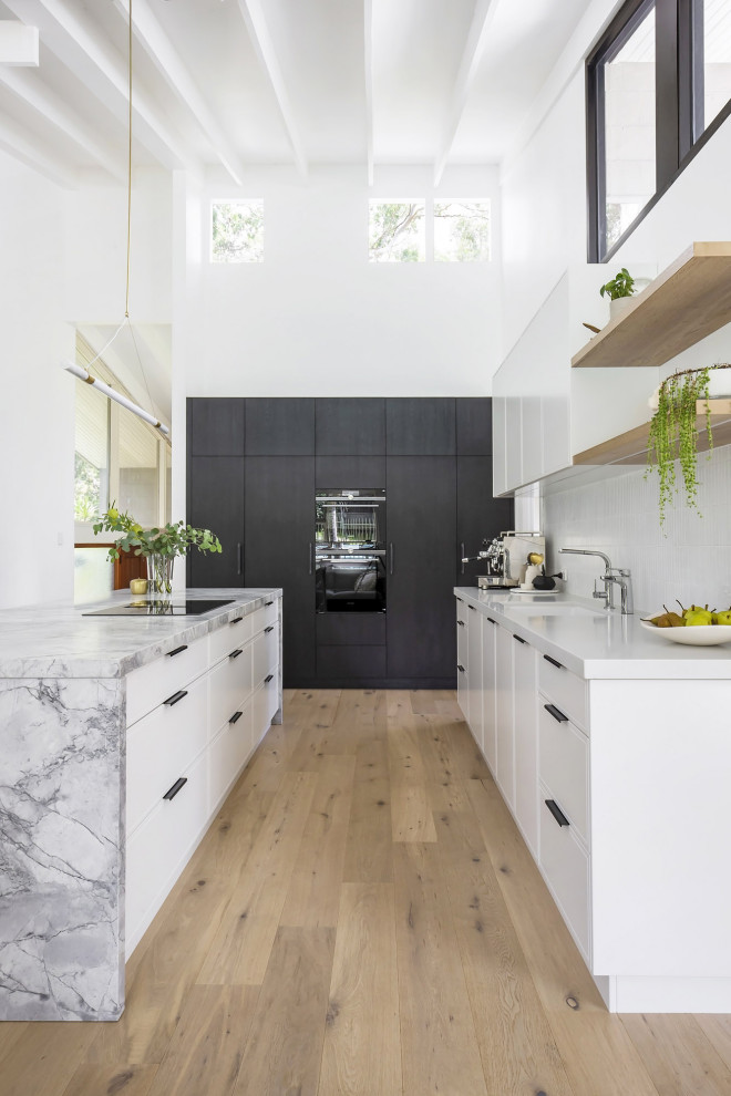 Photo of a mid-sized modern l-shaped open plan kitchen in Sydney with an undermount sink, flat-panel cabinets, dark wood cabinets, granite benchtops, white splashback, matchstick tile splashback, black appliances, light hardwood floors, with island, beige floor, grey benchtop and exposed beam.