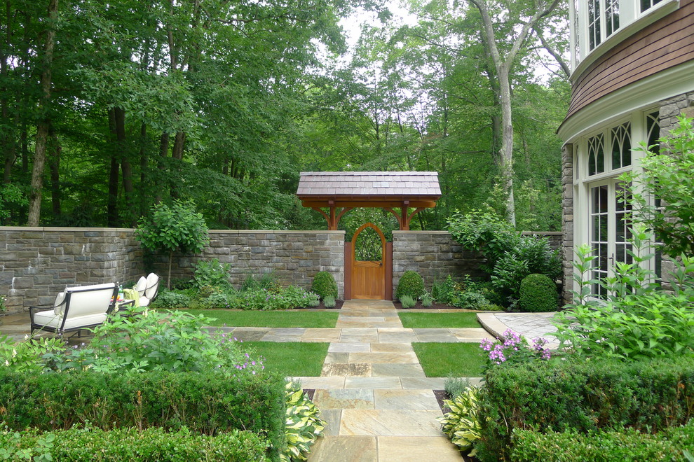 Large traditional backyard formal garden in New York with natural stone pavers and a garden path.