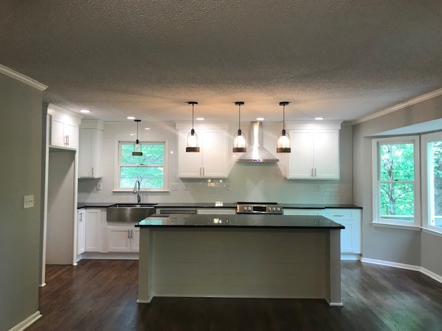 Inspiration for a mid-sized transitional l-shaped medium tone wood floor and brown floor eat-in kitchen remodel with a farmhouse sink, shaker cabinets, white cabinets, granite countertops, white backsplash, subway tile backsplash, stainless steel appliances, an island and black countertops