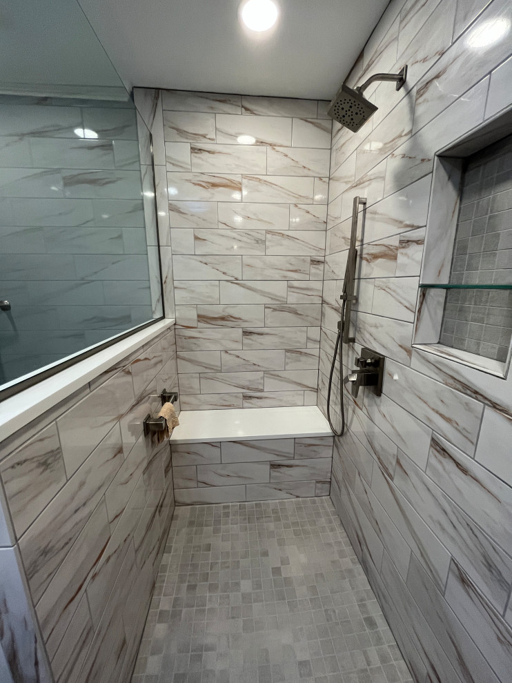 Photo of a large traditional ensuite bathroom in Indianapolis with beaded cabinets, grey cabinets, a built-in shower, a one-piece toilet, multi-coloured tiles, porcelain tiles, grey walls, porcelain flooring, a submerged sink, granite worktops, white floors, an open shower, black worktops, a shower bench, double sinks and a built in vanity unit.