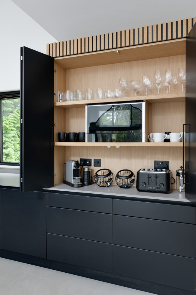 Inspiration for an expansive modern l-shaped eat-in kitchen in Hertfordshire with an integrated sink, flat-panel cabinets, black cabinets, quartzite benchtops, grey splashback, engineered quartz splashback, black appliances, porcelain floors, with island, grey floor, grey benchtop and vaulted.