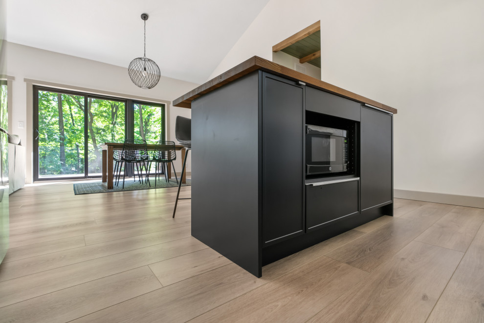 This is an example of a mid-sized contemporary l-shaped eat-in kitchen in St Louis with a single-bowl sink, flat-panel cabinets, black cabinets, marble benchtops, white splashback, ceramic splashback, stainless steel appliances, vinyl floors, with island, brown floor, grey benchtop and vaulted.