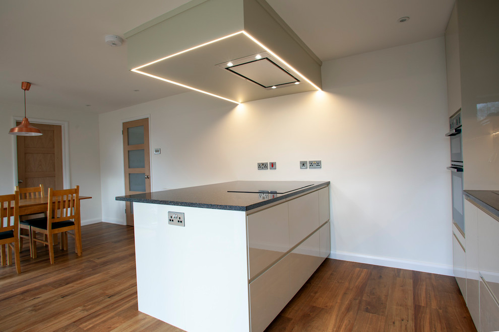This is an example of a mid-sized modern single-wall eat-in kitchen in Surrey with an integrated sink, flat-panel cabinets, beige cabinets, quartzite benchtops, multi-coloured splashback, stone tile splashback, panelled appliances, vinyl floors, with island and black benchtop.
