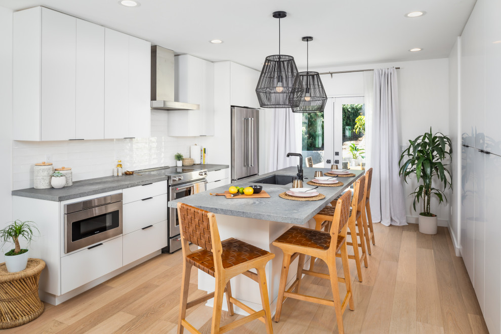 This is an example of a small contemporary single-wall eat-in kitchen in San Diego with an undermount sink, flat-panel cabinets, white cabinets, quartz benchtops, white splashback, glass tile splashback, stainless steel appliances, medium hardwood floors, with island and grey benchtop.