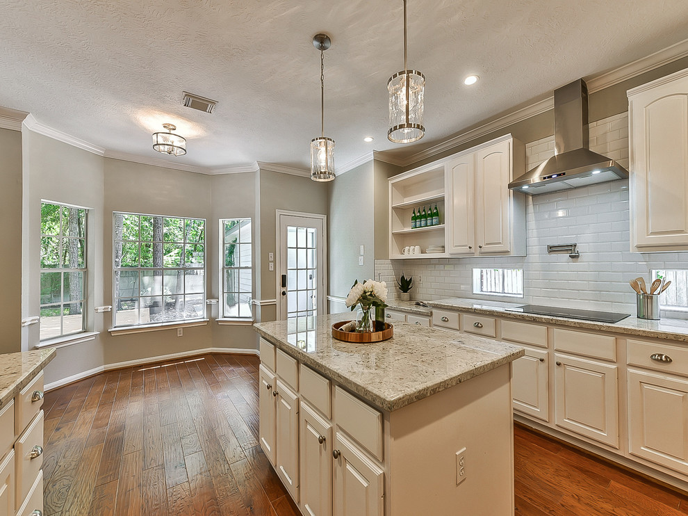 This is an example of a mid-sized transitional u-shaped eat-in kitchen in Houston with an undermount sink, white cabinets, granite benchtops, white splashback, subway tile splashback, stainless steel appliances, medium hardwood floors, with island, orange floor, white benchtop and raised-panel cabinets.