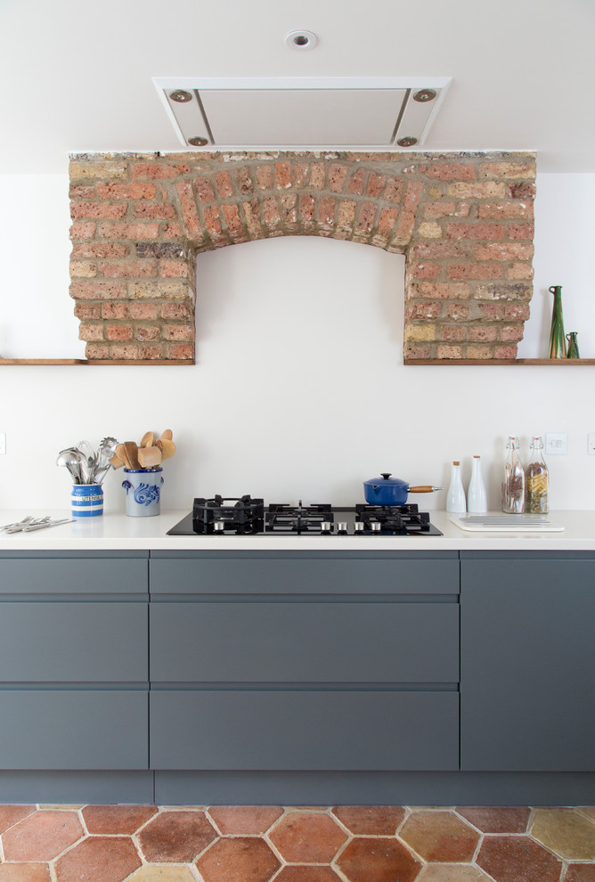 Photo of a large contemporary l-shaped eat-in kitchen in London with a double-bowl sink, flat-panel cabinets, blue cabinets, solid surface benchtops, white splashback, stainless steel appliances, terra-cotta floors, with island, multi-coloured floor and white benchtop.