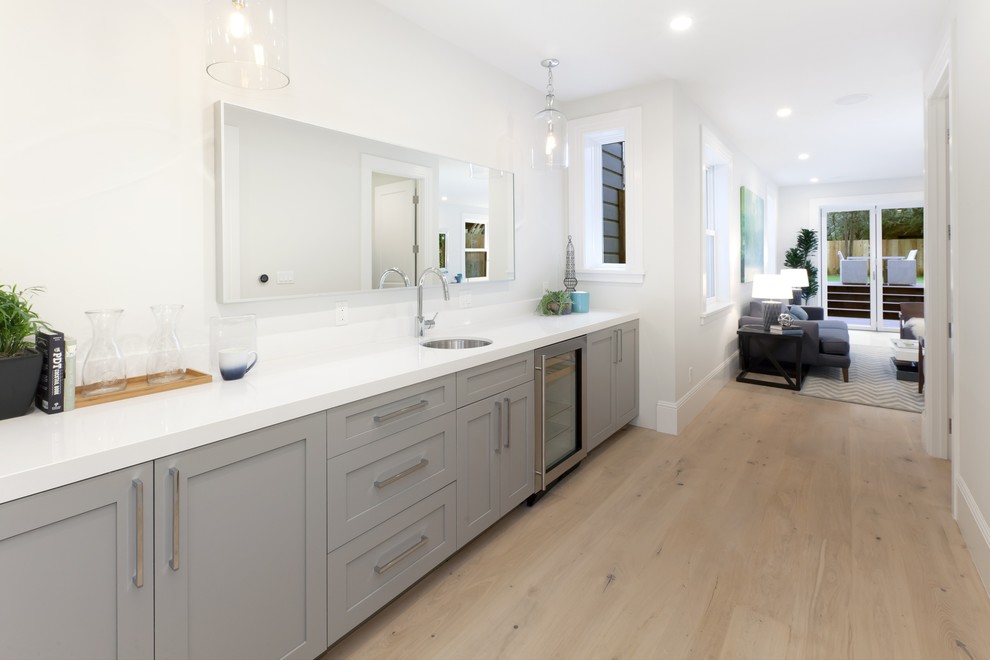 Photo of a large transitional single-wall wet bar in San Francisco with an undermount sink, shaker cabinets, grey cabinets, quartz benchtops and light hardwood floors.
