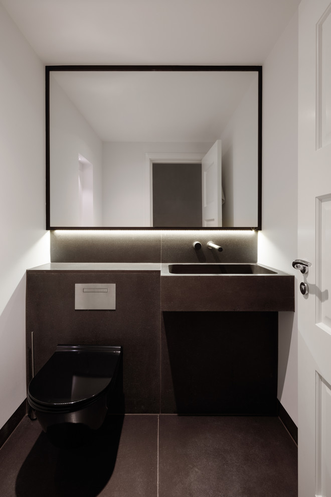 Inspiration for a mid-sized contemporary powder room in London with a wall-mount toilet, black tile, limestone, black walls, limestone floors, an integrated sink, limestone benchtops and black floor.