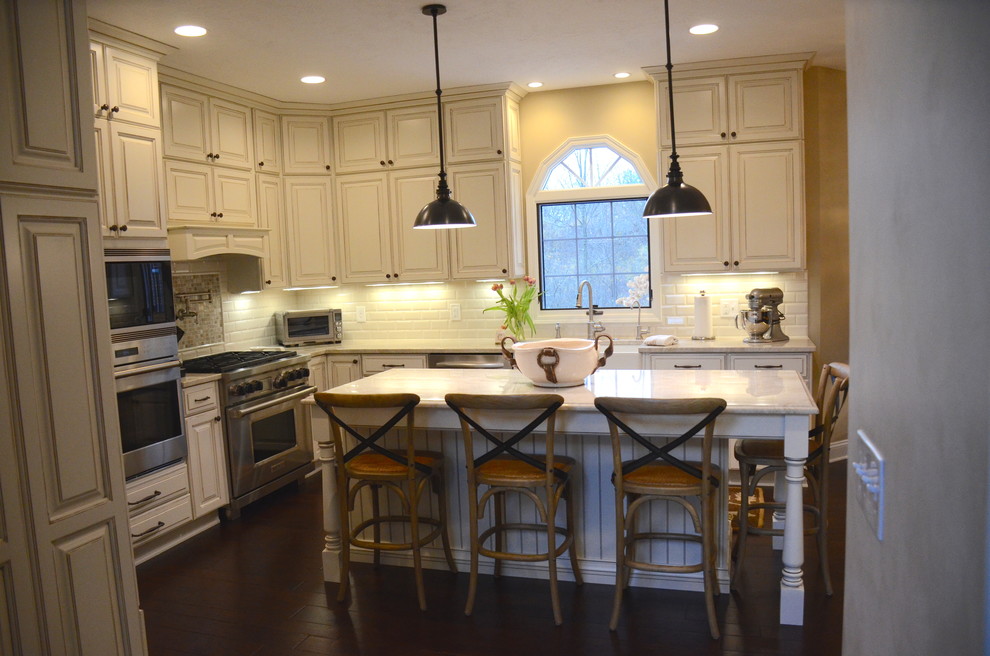 Inspiration for a large transitional l-shaped dark wood floor open concept kitchen remodel in Cleveland with a farmhouse sink, raised-panel cabinets, white cabinets, quartzite countertops, white backsplash, ceramic backsplash, stainless steel appliances and an island