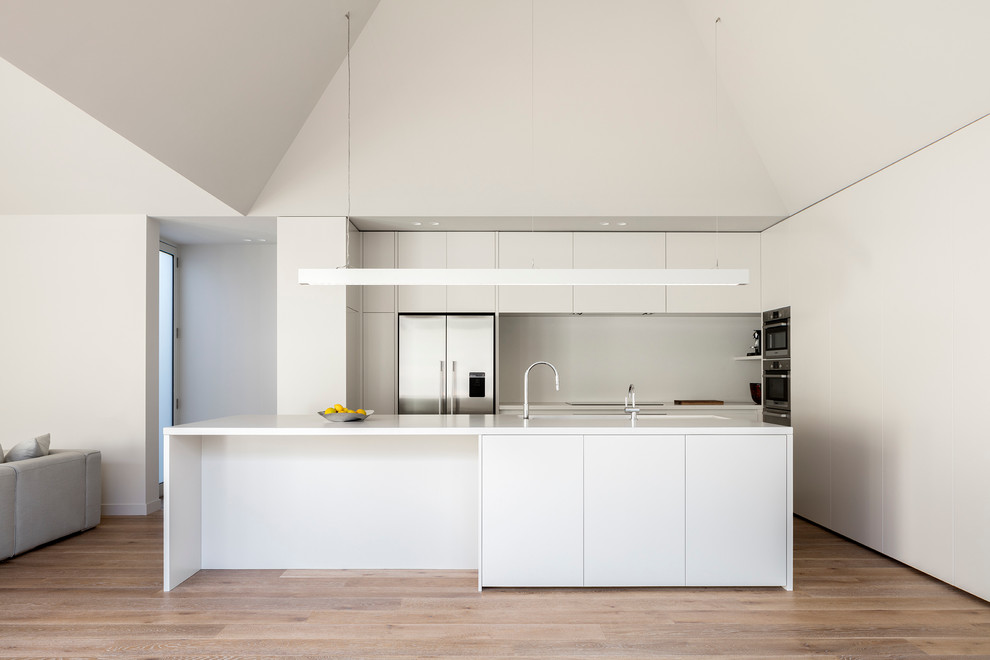 Photo of a modern galley eat-in kitchen in Melbourne with grey splashback, stainless steel appliances, with island, flat-panel cabinets and white cabinets.