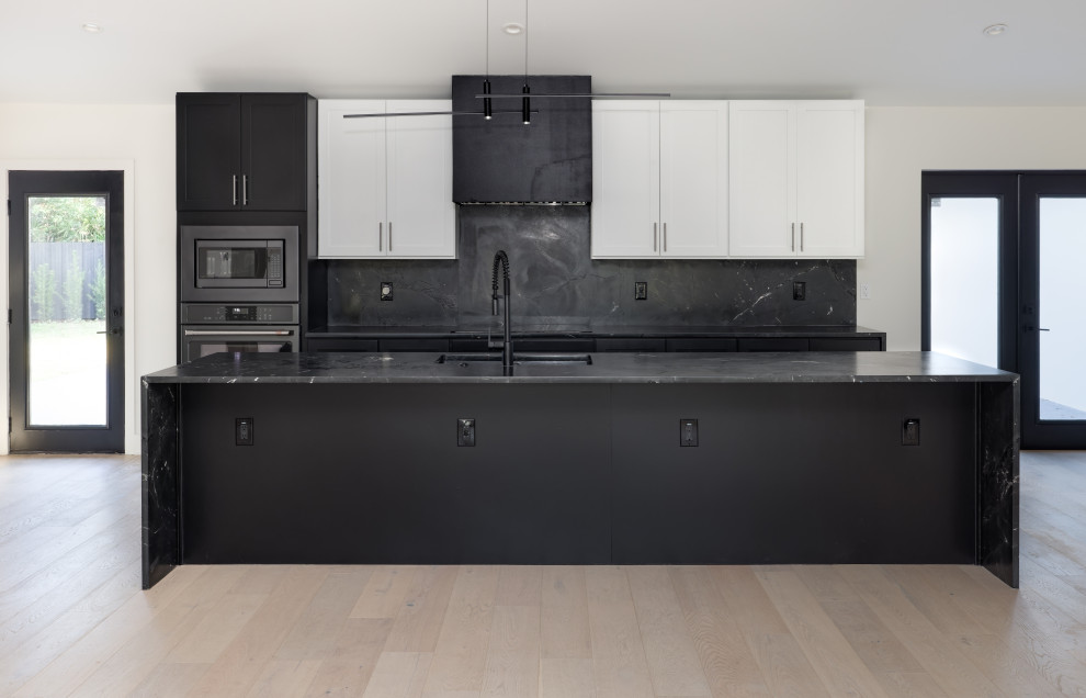 This is an example of a kitchen/diner in Orlando with a submerged sink, shaker cabinets, marble worktops, black splashback, marble splashback, black appliances, light hardwood flooring, an island, black worktops and a vaulted ceiling.