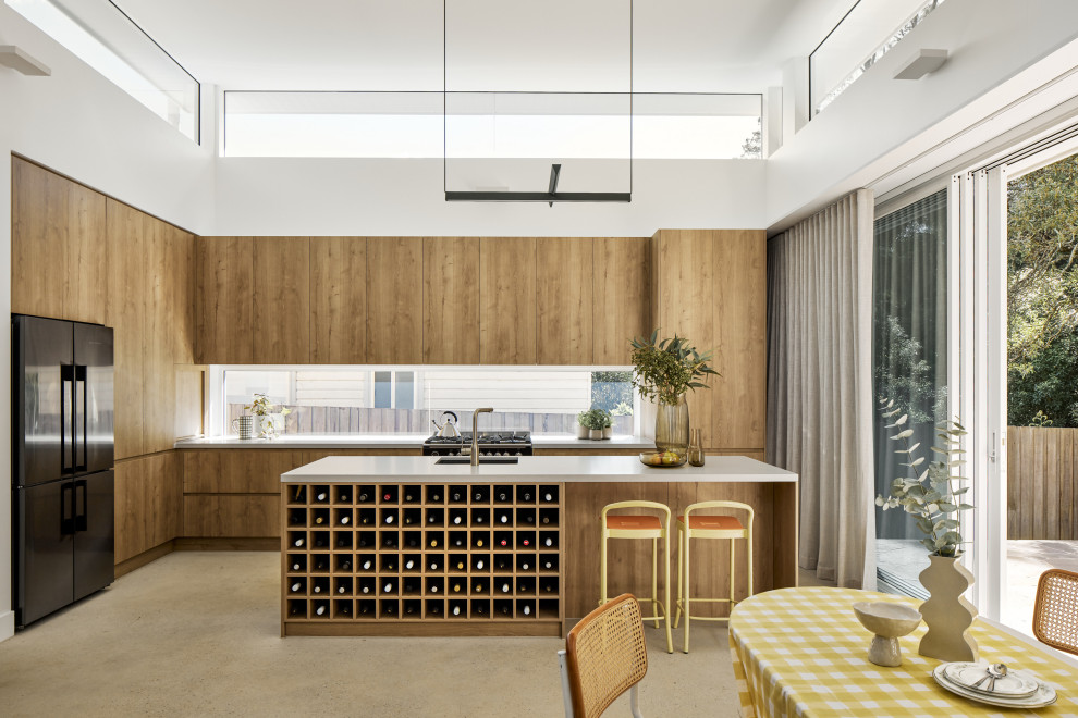 Photo of a mid-sized midcentury l-shaped eat-in kitchen in Sydney with an undermount sink, medium wood cabinets, quartz benchtops, black appliances, concrete floors, with island, grey floor, grey benchtop, flat-panel cabinets and window splashback.