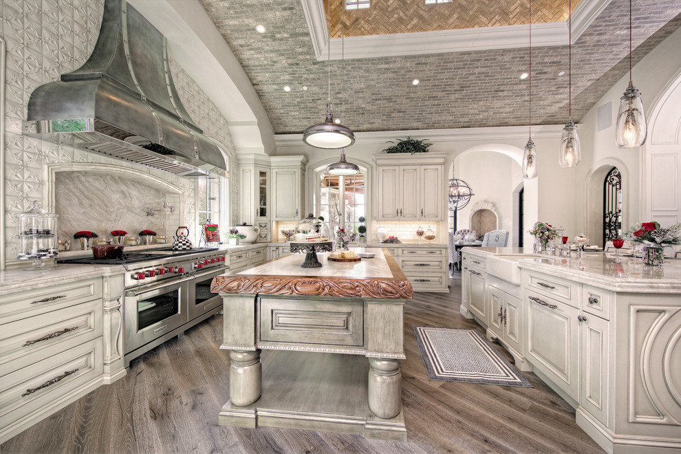 Design ideas for an expansive mediterranean u-shaped eat-in kitchen in Phoenix with a farmhouse sink, recessed-panel cabinets, medium wood cabinets, beige splashback, mosaic tile splashback, stainless steel appliances, medium hardwood floors, multiple islands and marble benchtops.