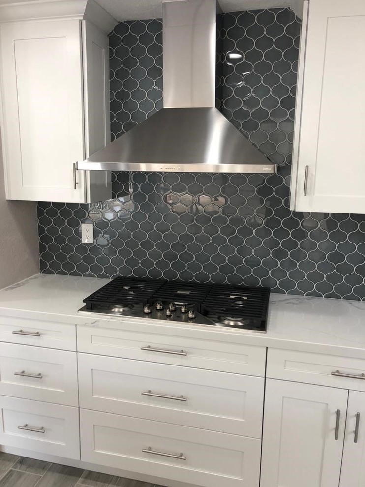 Inspiration for a large modern l-shaped open plan kitchen in San Diego with a farmhouse sink, shaker cabinets, white cabinets, marble benchtops, blue splashback, ceramic splashback, stainless steel appliances, medium hardwood floors, with island, grey floor and white benchtop.