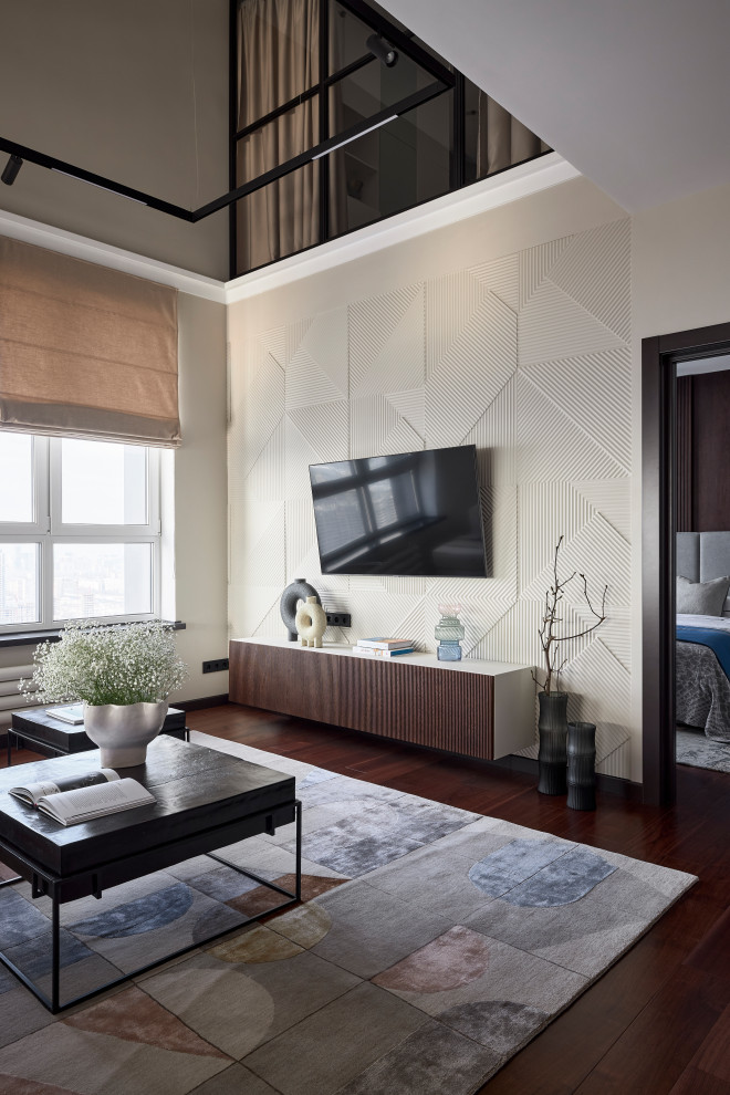 На фото: двухуровневая гостиная комната в современном стиле с бежевыми стенами, темным паркетным полом, телевизором на стене, коричневым полом и панелями на части стены с