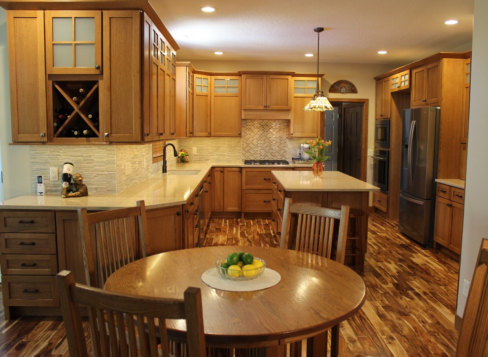 This is an example of a large arts and crafts u-shaped open plan kitchen in Other with an undermount sink, flat-panel cabinets, medium wood cabinets, quartz benchtops, beige splashback, stone tile splashback, stainless steel appliances, medium hardwood floors, with island, brown floor and beige benchtop.
