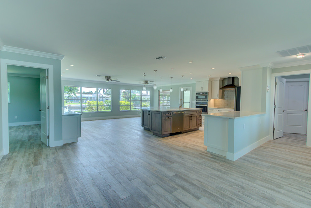 Example of a large transitional l-shaped ceramic tile and gray floor home design design with an undermount sink, shaker cabinets, white cabinets, recycled glass countertops, blue backsplash, glass tile backsplash, stainless steel appliances, an island and white countertops