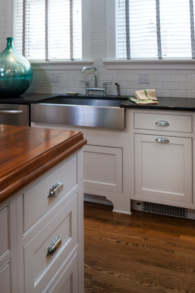 Example of a mid-sized transitional u-shaped medium tone wood floor open concept kitchen design with a farmhouse sink, shaker cabinets, white cabinets, wood countertops, white backsplash, porcelain backsplash, stainless steel appliances and an island