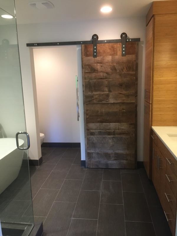 Expansive contemporary master bathroom in Portland with flat-panel cabinets, medium wood cabinets, a freestanding tub, an alcove shower, a two-piece toilet, white tile, glass tile, white walls, ceramic floors, an undermount sink, solid surface benchtops, brown floor and a hinged shower door.