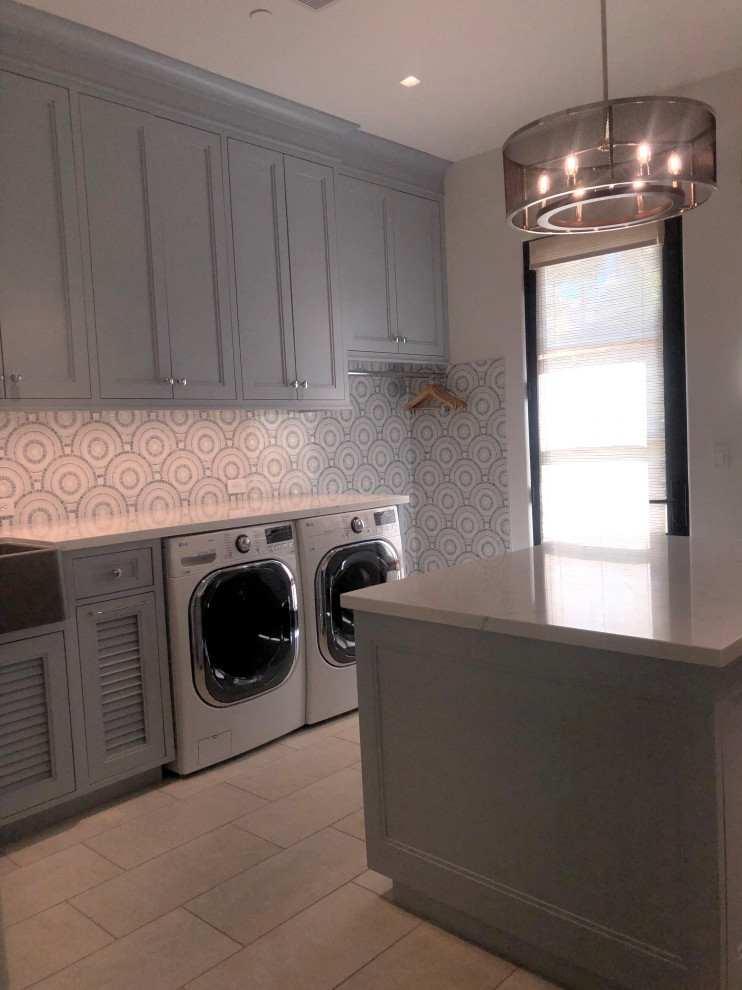 Large transitional u-shaped dedicated laundry room in San Diego with a farmhouse sink, shaker cabinets, blue cabinets, quartz benchtops, blue splashback, mosaic tile splashback, white walls, porcelain floors, a side-by-side washer and dryer, grey floor and white benchtop.