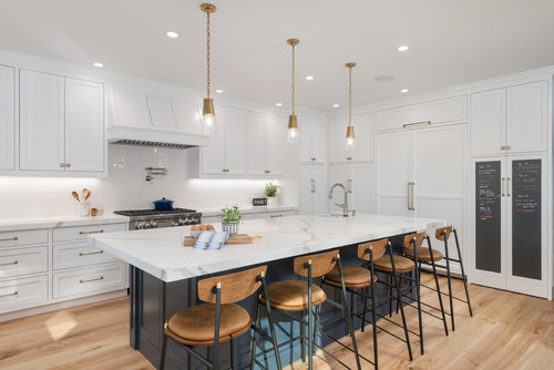 Bright modern kitchen featuring white shaker kitchen cabinets in Mississauga, a navy blue waterfall island with marble-look countertop, brass pendant lights, and six wood-and-metal bar stools.