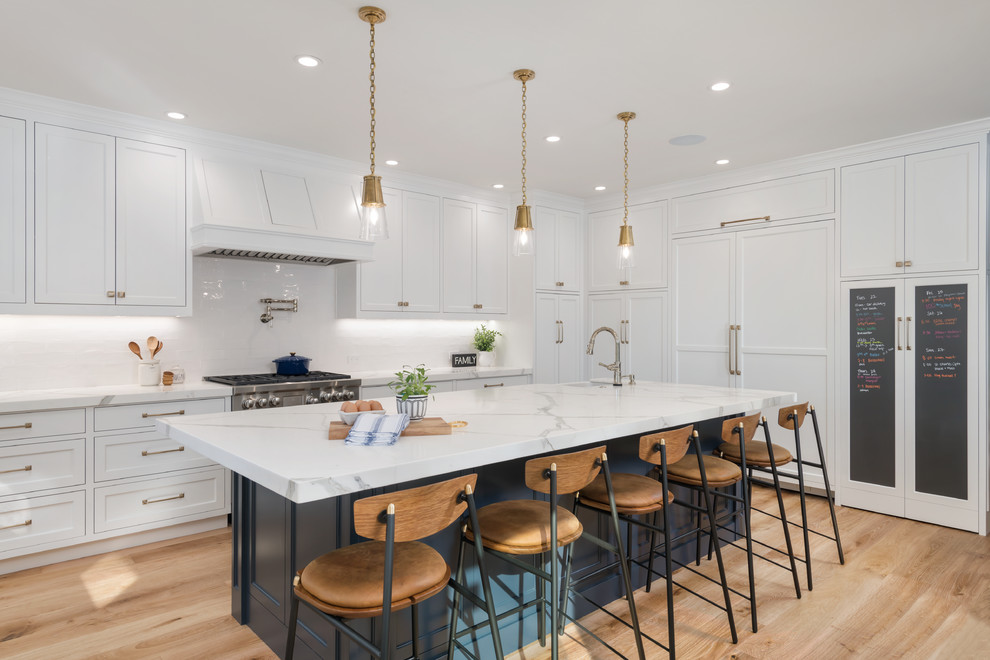 Inspiration for a large country l-shaped kitchen in San Francisco with a farmhouse sink, beaded inset cabinets, white cabinets, marble benchtops, white splashback, ceramic splashback, panelled appliances, medium hardwood floors, with island, brown floor and white benchtop.