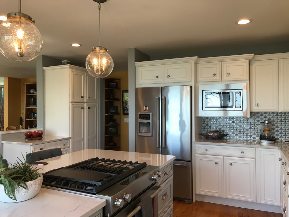 Eat-in kitchen - mid-sized transitional l-shaped medium tone wood floor and brown floor eat-in kitchen idea with a farmhouse sink, recessed-panel cabinets, white cabinets, marble countertops, gray backsplash, mosaic tile backsplash, stainless steel appliances and an island
