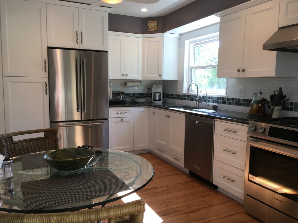 Example of a mid-sized transitional l-shaped light wood floor enclosed kitchen design with an undermount sink, flat-panel cabinets, white cabinets, granite countertops, white backsplash, subway tile backsplash, stainless steel appliances and no island