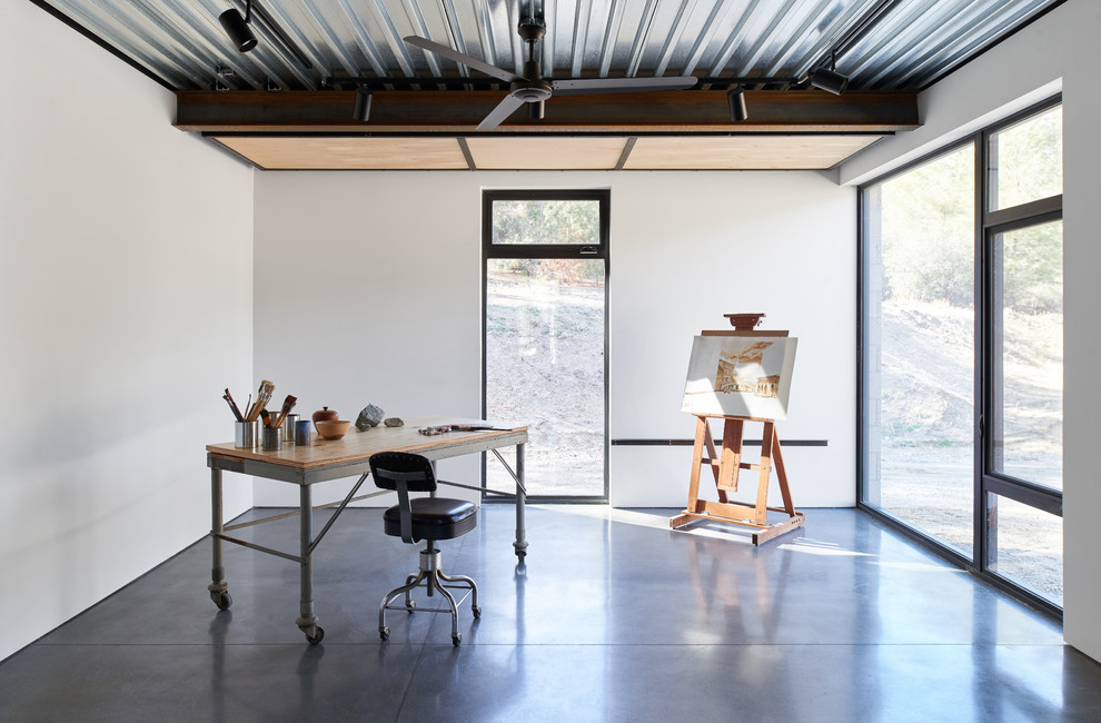 Photo of an industrial home office in Los Angeles with white walls, concrete floors, a freestanding desk and grey floor.