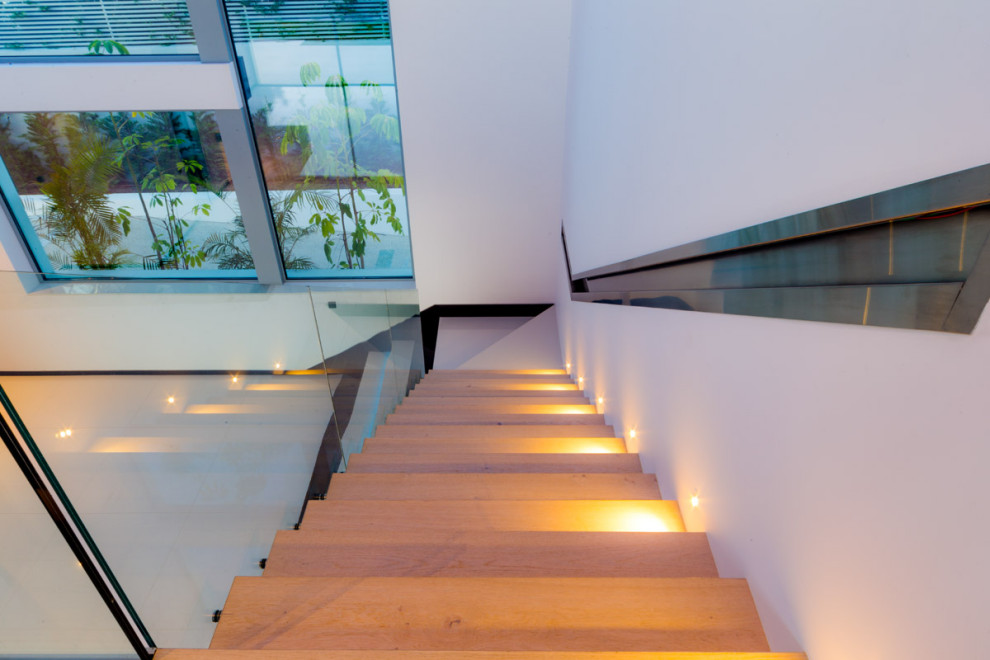 Réalisation d'un escalier flottant design avec des marches en bois, des contremarches en bois et un garde-corps en verre.