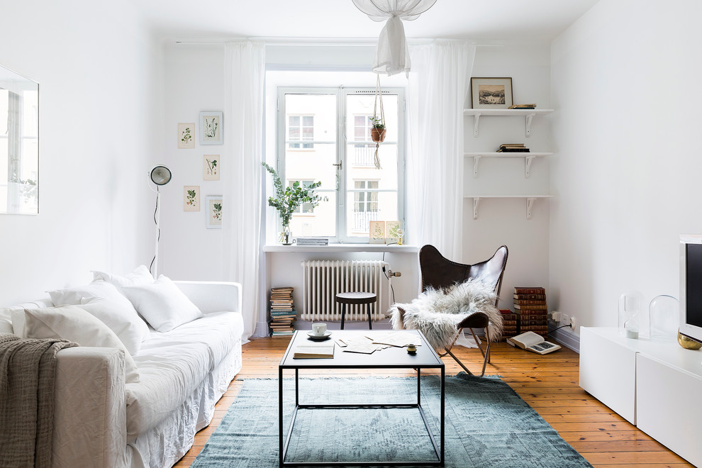 Mid-sized scandinavian living room in Stockholm with white walls, medium hardwood floors, a freestanding tv and no fireplace.