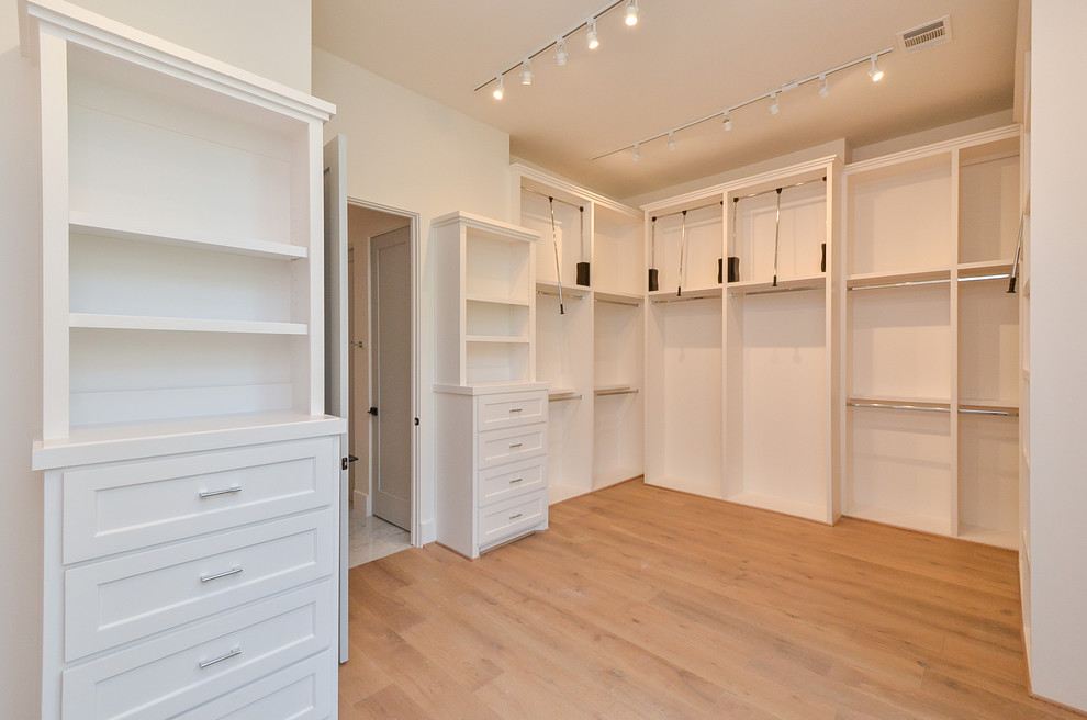 Inspiration for a large traditional gender-neutral walk-in wardrobe in Houston with open cabinets, white cabinets, light hardwood floors and beige floor.