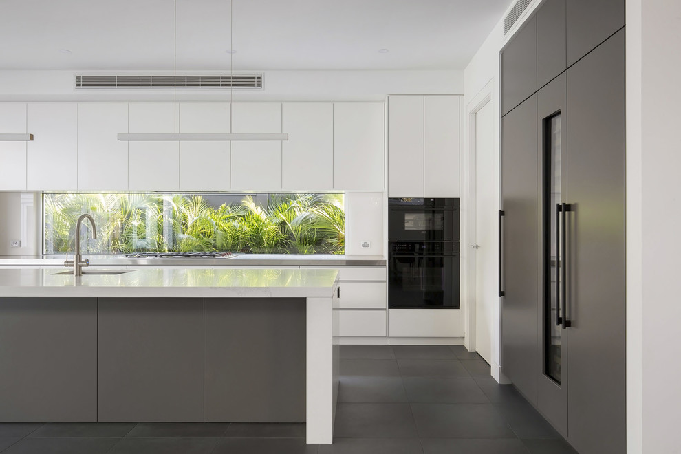 This is an example of a large modern l-shaped open plan kitchen in Sydney with an undermount sink, flat-panel cabinets, grey cabinets, quartz benchtops, white splashback, window splashback, black appliances, porcelain floors, with island, grey floor and white benchtop.