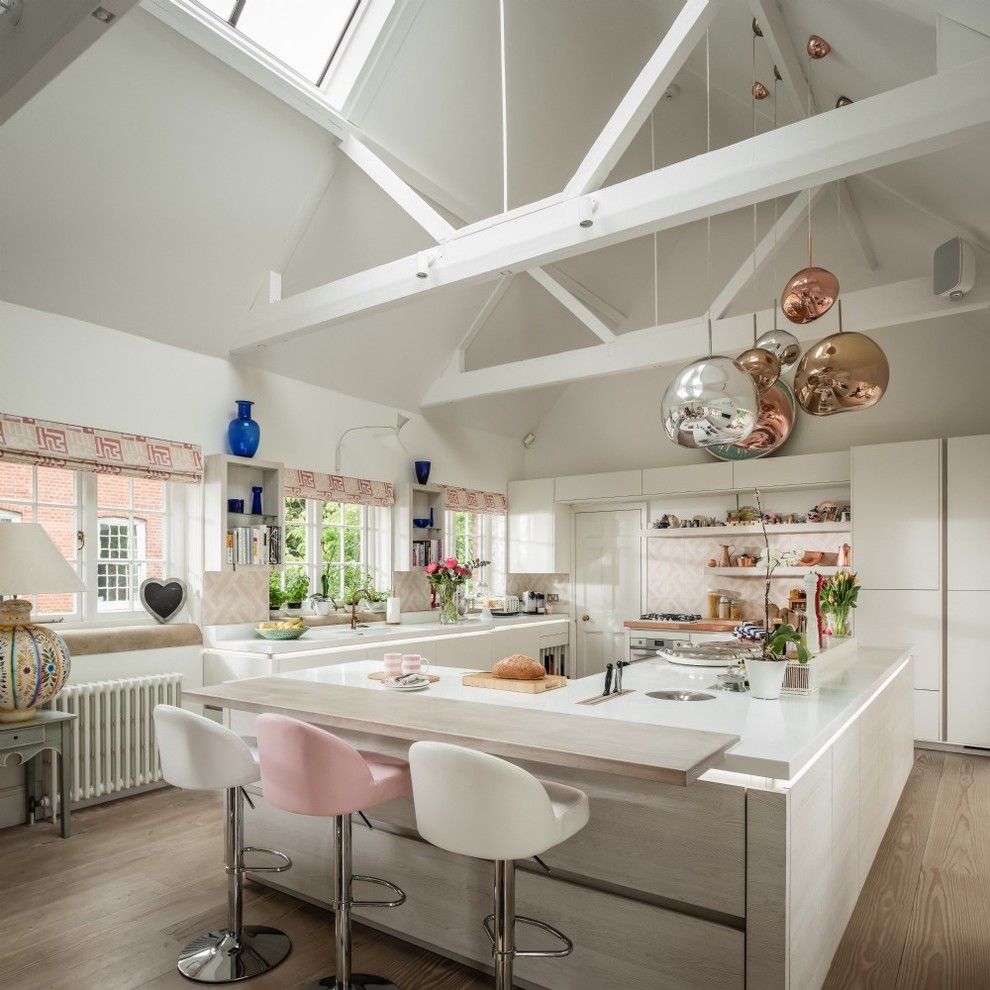 Mid-sized eclectic kitchen in Hampshire with flat-panel cabinets, white cabinets, pink splashback, medium hardwood floors, with island and white benchtop.