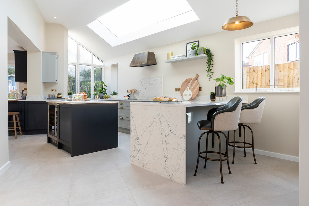 This is an example of a large scandinavian galley eat-in kitchen in West Midlands with a drop-in sink, shaker cabinets, grey cabinets, marble benchtops, black appliances, ceramic floors, with island, white floor and white benchtop.