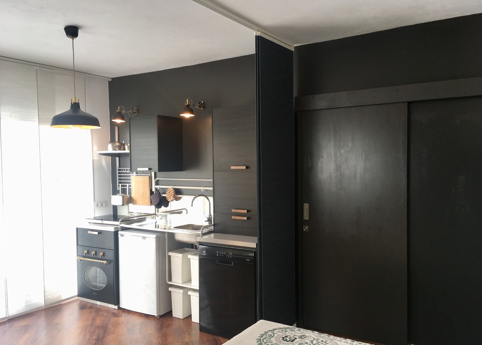 Photo of a small modern single-wall eat-in kitchen in Other with flat-panel cabinets, black cabinets, stainless steel benchtops, mirror splashback, black appliances, vinyl floors, no island and a drop-in sink.