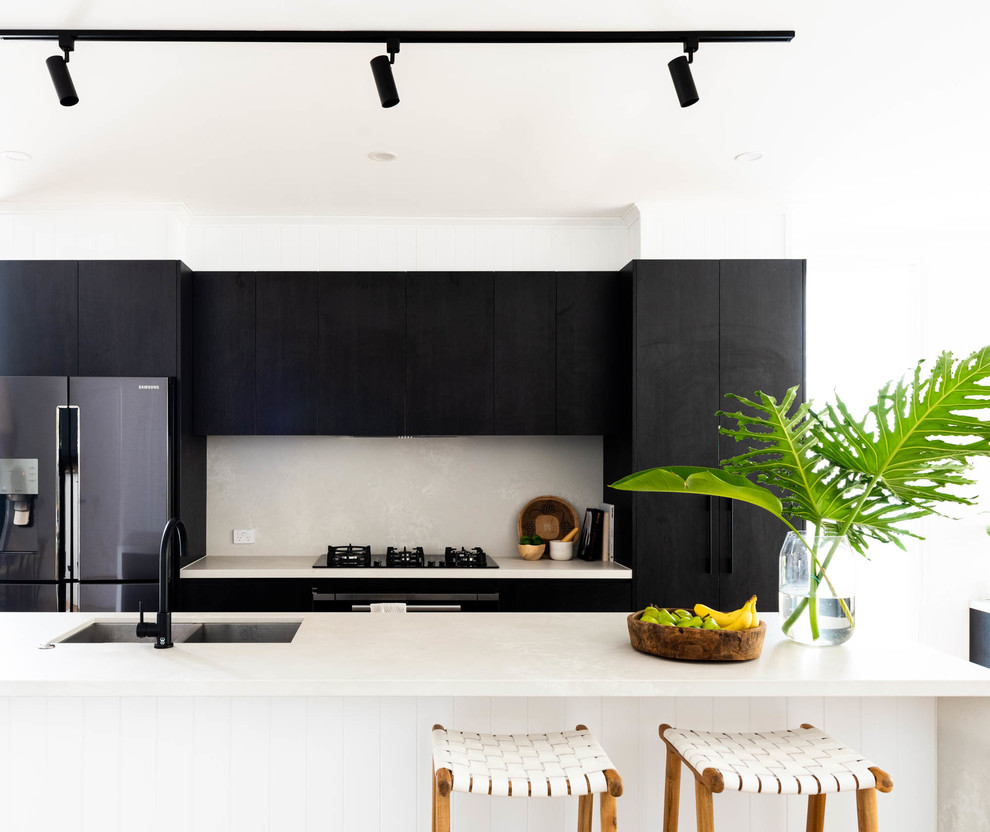 Inspiration for a beach style galley kitchen in Brisbane with a double-bowl sink, flat-panel cabinets, black cabinets, white splashback, stainless steel appliances, with island and white benchtop.