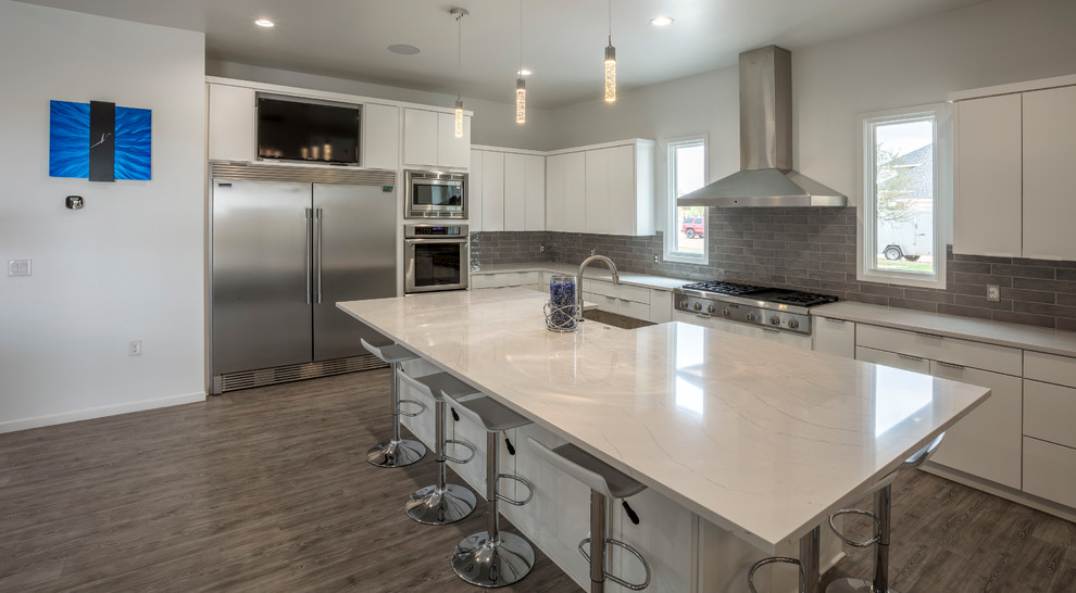 Large transitional l-shaped vinyl floor eat-in kitchen photo with flat-panel cabinets, white cabinets, quartzite countertops, gray backsplash, glass tile backsplash, stainless steel appliances and an island