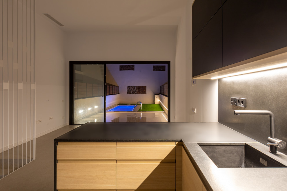 Inspiration for a large contemporary u-shaped beige floor and tray ceiling open concept kitchen remodel in Barcelona with a single-bowl sink, flat-panel cabinets, black cabinets, black backsplash, black appliances, a peninsula and black countertops