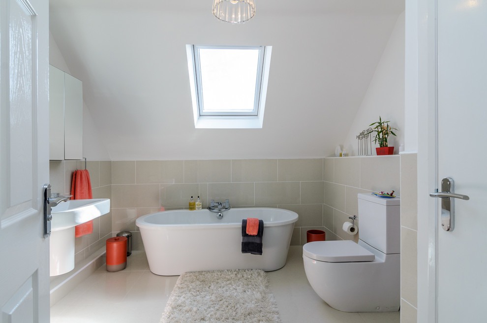 Photo of a mid-sized modern kids bathroom in Belfast with a wall-mount sink, flat-panel cabinets, white cabinets, a freestanding tub, a one-piece toilet, beige tile, ceramic tile and white walls.
