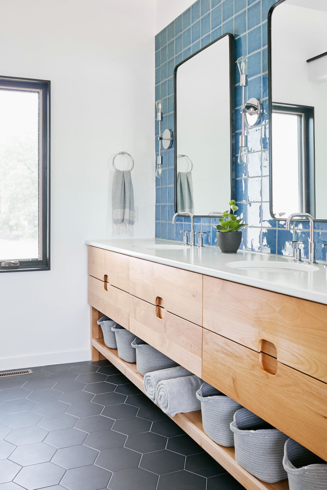 Пример оригинального дизайна: ванная комната в стиле ретро с плоскими фасадами, фасадами цвета дерева среднего тона, синей плиткой, белыми стенами, врезной раковиной, черным полом, белой столешницей, тумбой под две раковины и встроенной тумбой