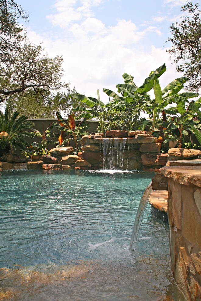 Inspiration for a mid-sized tropical backyard custom-shaped natural pool in Austin with natural stone pavers and a hot tub.