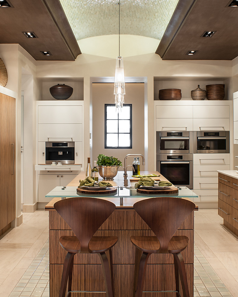 This is an example of a large contemporary u-shaped open plan kitchen in Phoenix with flat-panel cabinets, medium wood cabinets, quartz benchtops, white splashback, stainless steel appliances, limestone floors, with island and an undermount sink.