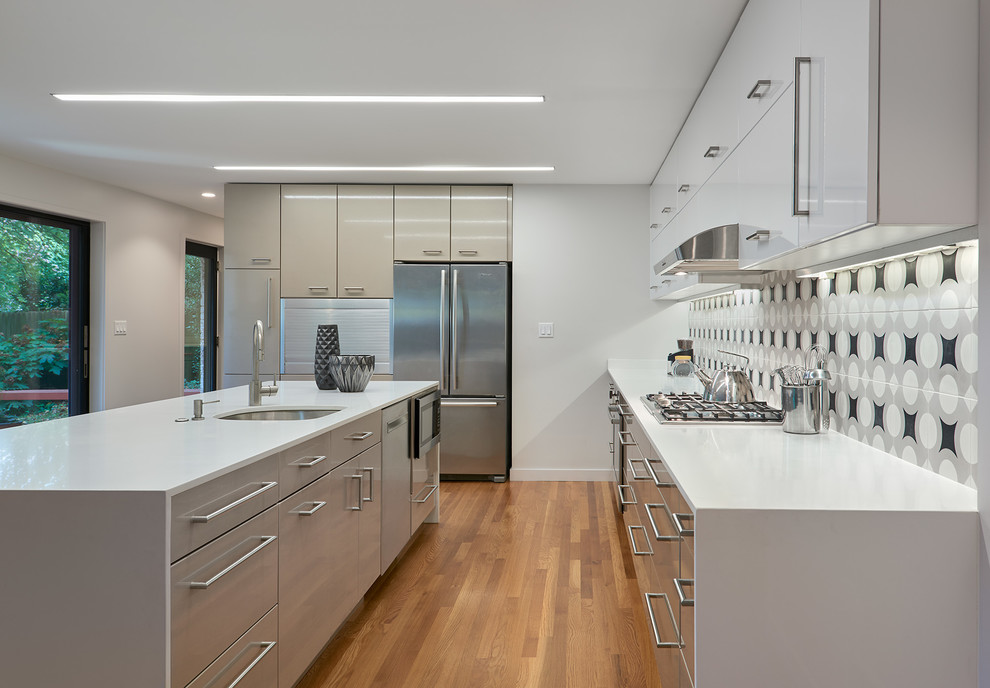 Large modern l-shaped open plan kitchen in DC Metro with an undermount sink, flat-panel cabinets, white cabinets, quartzite benchtops, black splashback, ceramic splashback, stainless steel appliances, medium hardwood floors, with island and brown floor.