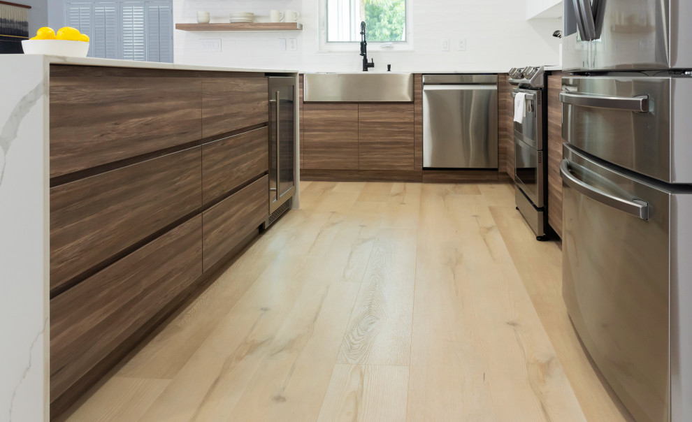 Example of a mid-sized l-shaped laminate floor open concept kitchen design in Miami with a farmhouse sink, flat-panel cabinets, medium tone wood cabinets, quartz countertops, white backsplash, subway tile backsplash, stainless steel appliances, an island and white countertops