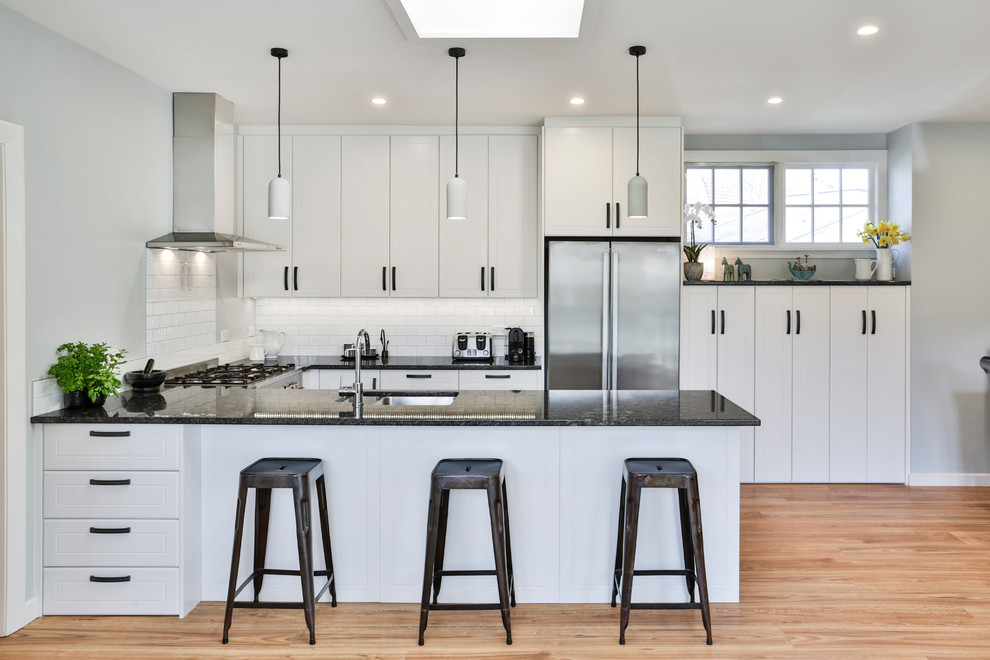 Inspiration for a mid-sized transitional u-shaped eat-in kitchen in Christchurch with an undermount sink, white cabinets, granite benchtops, white splashback, subway tile splashback, stainless steel appliances, medium hardwood floors, black benchtop, shaker cabinets, a peninsula and beige floor.
