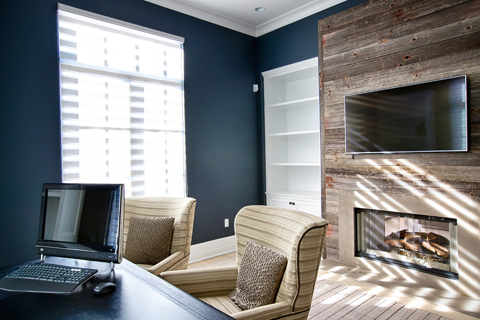 This is an example of a mid-sized transitional home office in New York with blue walls, medium hardwood floors, a standard fireplace, a wood fireplace surround, a freestanding desk and brown floor.