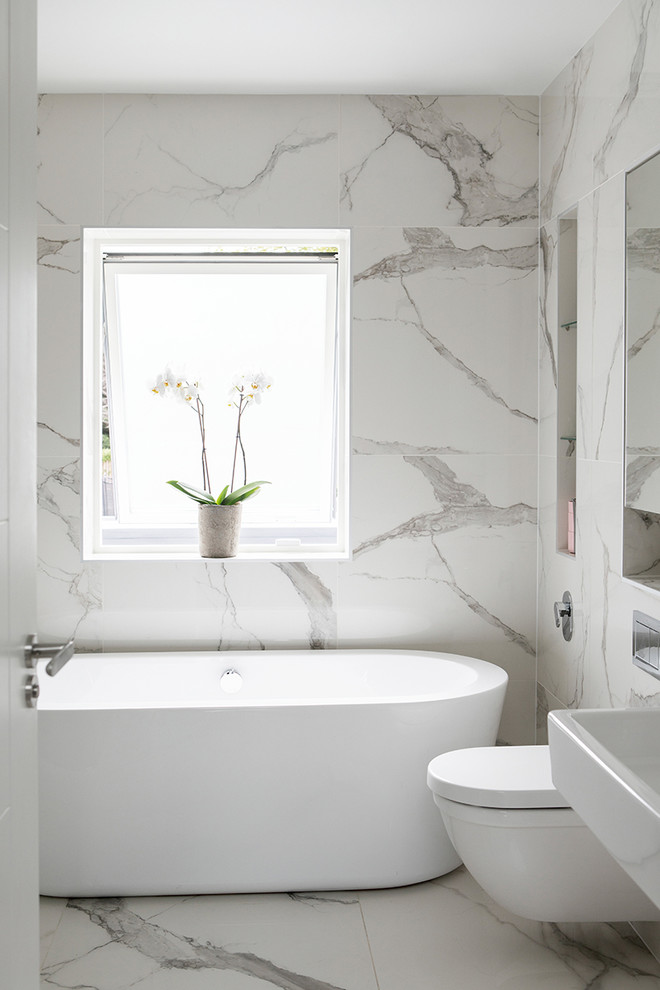 Photo of a contemporary bathroom in Dublin with a freestanding tub, white tile, a wall-mount sink and white floor.